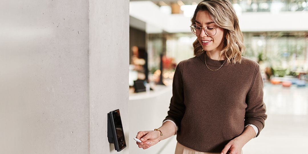 Frau im Empfangsbereich einer Firma hält Ausweis an Zeiterfassungsterminal IF-5735 von Interflex