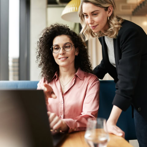 Zwei Frauen am Tisch blicken in den Laptop