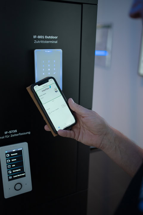 A person holds a smartphone to an access terminal on a product pedestal.