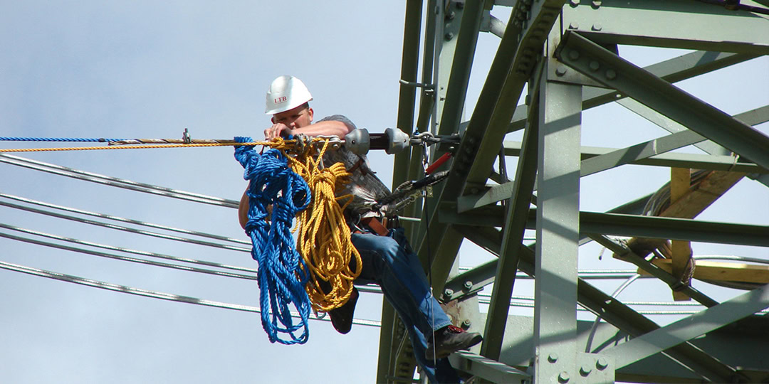 Worker with a safety helmet performs maintenance work on a power pole.