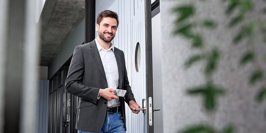Smiling man opens door with smartphone thanks to Interflex Opendor technology.