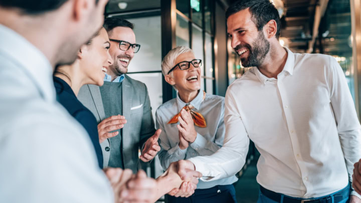 Group of laughing people, two people shake hands