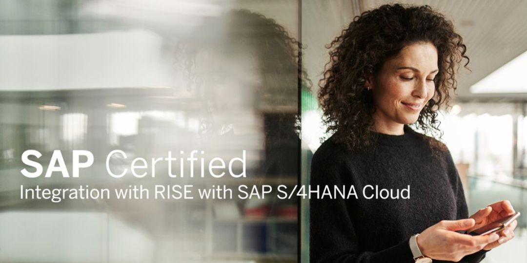 A woman leans against a glass wall in the office building and smiles at her smartphone.