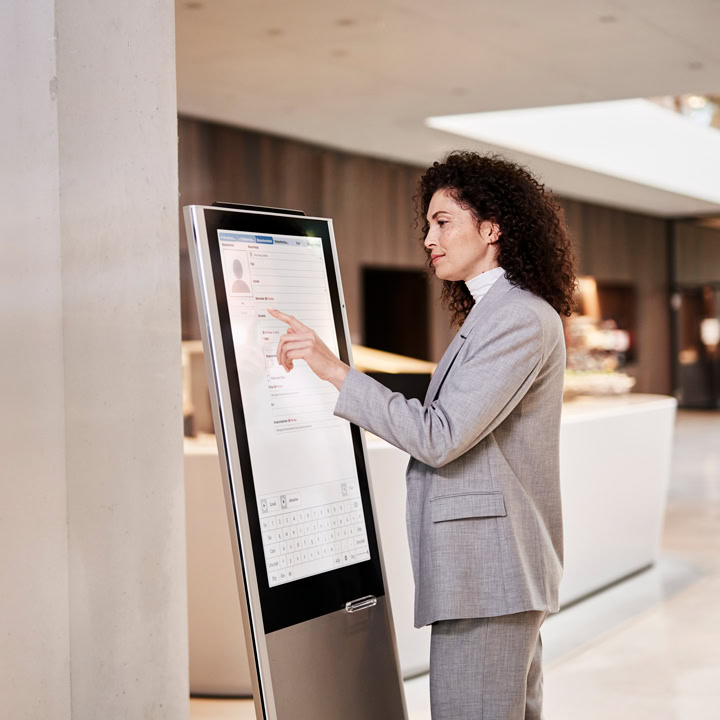 Frau im Eingangsbereich eines Gebäudes am digitalen Selbstanmeldungs-Kiosk
