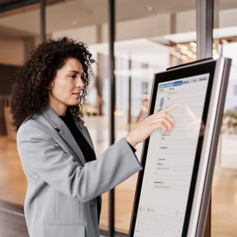 Frau im Windfang eines Gebäudes am digitalen Selbstanmeldungs-Kiosk