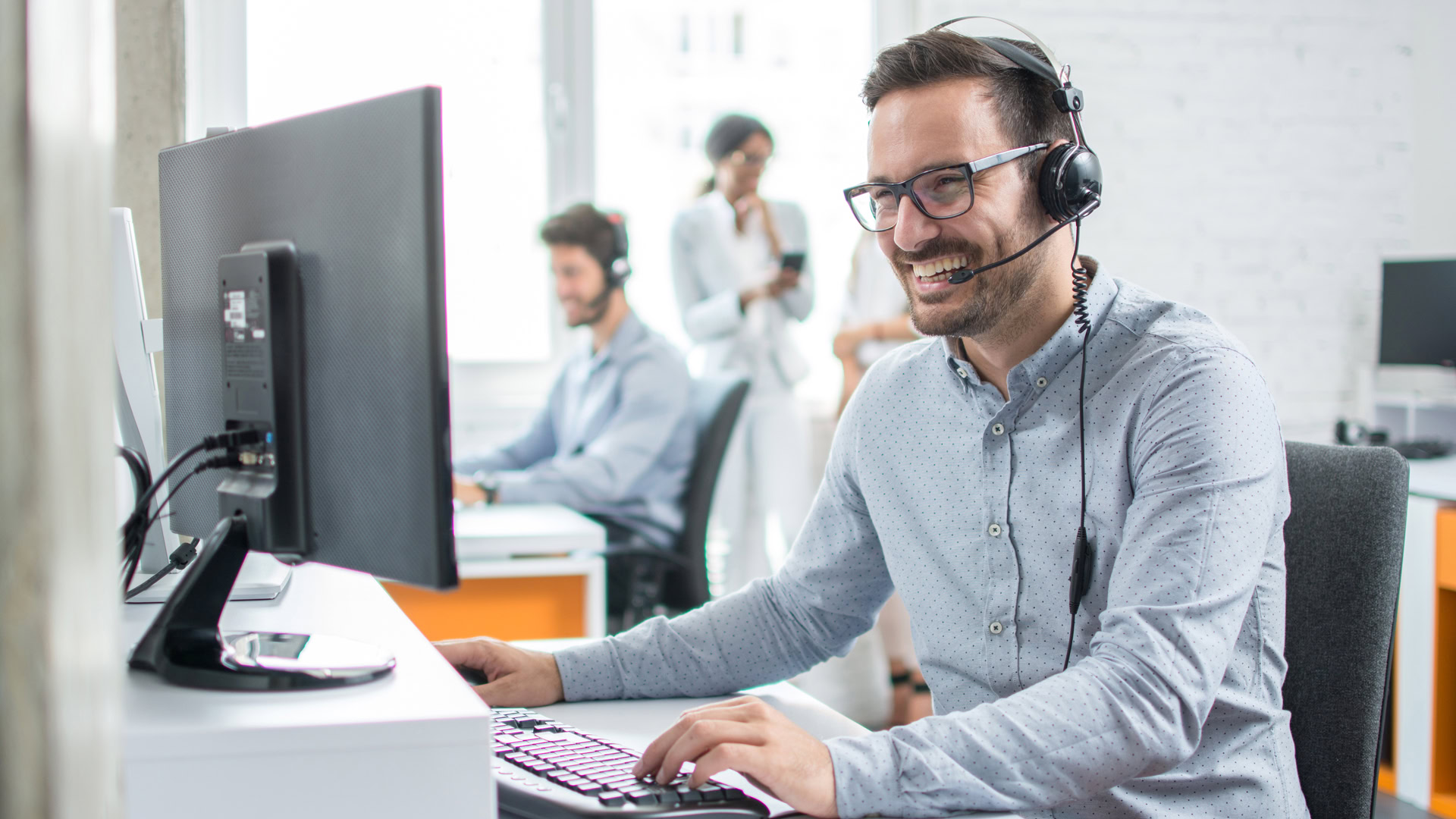 Call centre employee at his desk, looking at the monitor and laughing