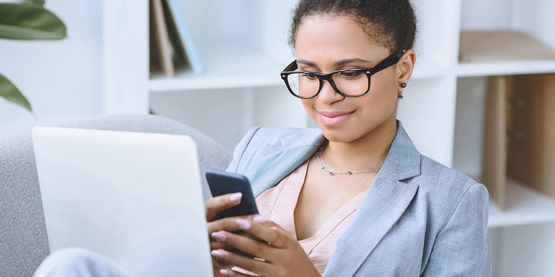 Woman sits relaxed in an armchair and looks smilingly at her smartphone.