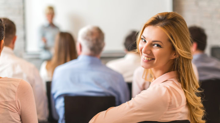 Frau während Seminar dreht sich lächelnd zum Betrachter