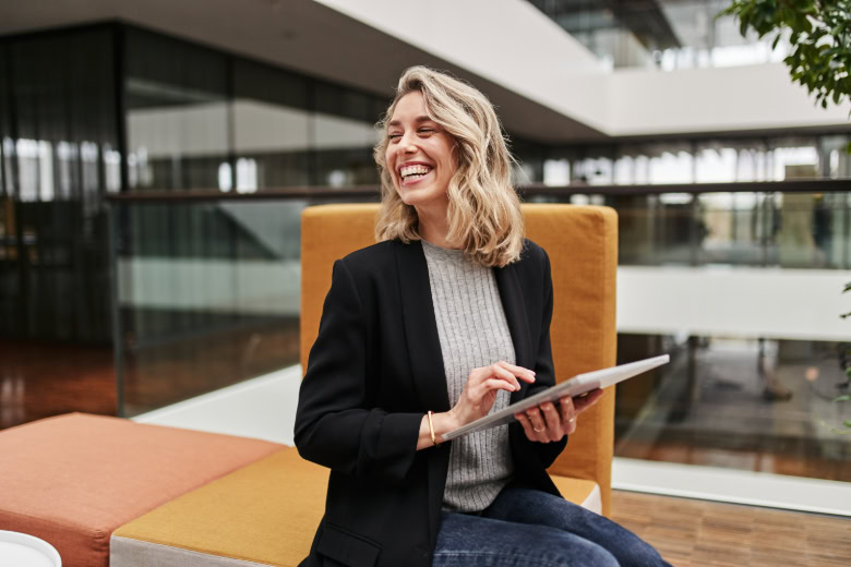 Vrouw die lachend zit op moderne lounge meubels en een tablet in haar handen houdt